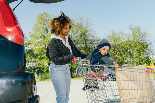Mother with child in shopping cart reaching for groceries