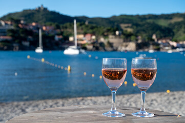 Glasses of rose Collioure AOC wine in sunlights with view on old town Collioure, colorful houses, church, castle and beaches, Occitanie, France, tourists destination