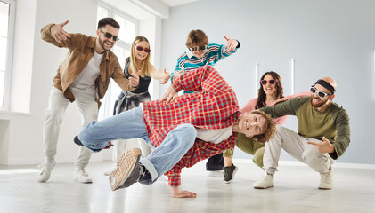 Group of happy cheerful people in casual clothes enjoying modern hip hop music and training at a break dance studio. Young man practicing dynamic breakdance elements together with fellow dancers
