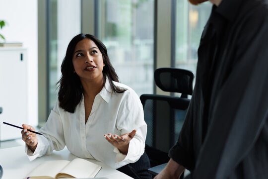Young latin female employee talking with partial colleague in office