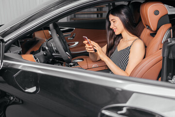 Young attractive asian woman using phone while sitting in a luxury car front sea