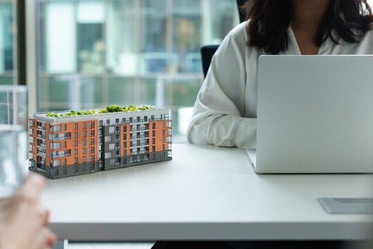 Cropped real estate agent typing laptop at desk with new house model