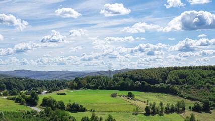Countryside panorama with green fields, hills, and forest. Scenic rural landscape under a blue sky with clouds.