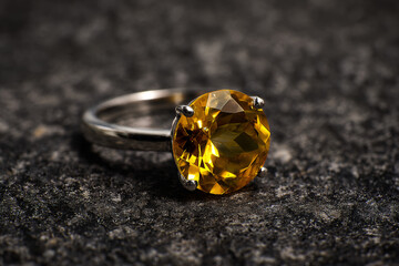 A close-up of a silver ring with a large brilliant yellow octagonal gemstone on dark textured surface
