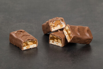 Chocolate bar. Nougat, caramel with peanuts, in chocolate glaze. Dark background. Close up	