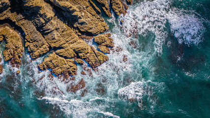 Ocean waves hitting rugged rocky shore seen from above with foamy white water and clear blue sea powerful coastal landscape and nature scenery