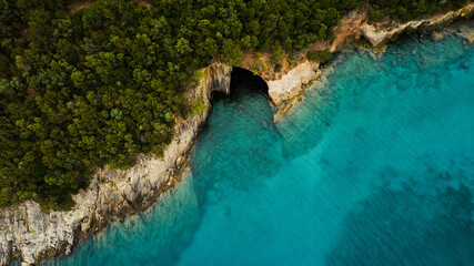Aerial view of sea cave along rocky coastline with turquoise blue water and dense green forest dramatic natural landscape and travel photo spot