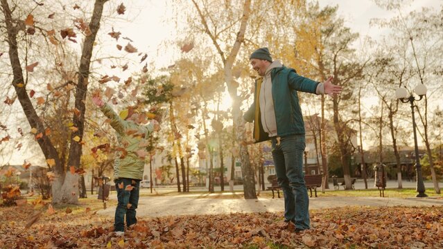 father and little child in an autumn park throw dry leaves up, happy family, live fun with dad, cheerful kid plays with foliage and parent hands throwing leaf fall, parental care of girl, nature walk