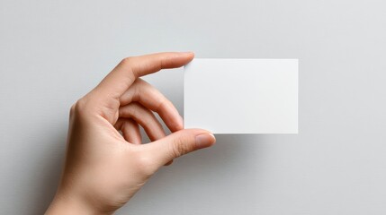 Fototapeta premium Elegant Hand Presenting a Blank White Business Card Mockup on a Neutral Gray Surface.