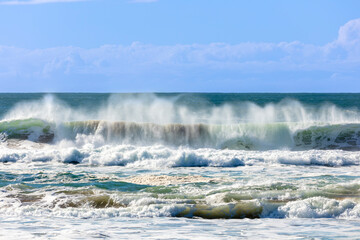 Photograph of waves from the Tasman Sea crashing onto Jones Beach against a blue sky near the town of Kiama Downs in the Illawarra region on the south coast of NSW, Australia.