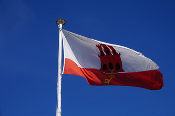 Gibraltarian Flag Waving Proudly Against Clear Blue Sky, The Red and White Banner of Gibraltar Fluttering in the Breeze on Top of Flagpole