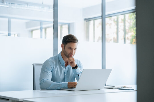 European focused young businessman entrepreneur sitting at desk working on financial project, looking thinking at screen. Latin business man ceo manager using laptop computer in office. Copy space