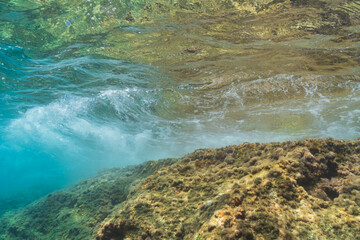 Dynamic underwater scene of a powerful wave breaking over a shallow reef in clear turquoise water in France.