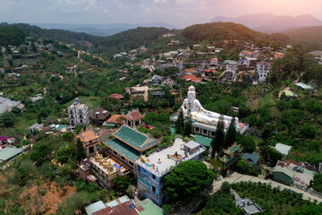 Naklejka premium High-angle view of the Tuyen Lam Lake complex in Da Lat, Vietnam, featuring colorful buildings and a large reclining Buddha statue, surrounded by green mountains and houses