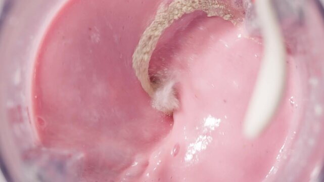 Strawberry and banana pink milkshake blended in blender with splashes. top view. slow motion. Healthy protein smoothie drink concept , food closeup. Protein powder falling in smoothie from spoon