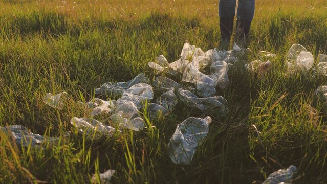 A woman in gloves collects garbage in a garbage bag at sunset, preserving a clean ecology of air and earth, the environment, preserving the earth, plastic garbage in the glare of the sun.