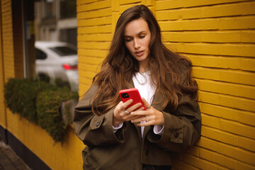 Outdoor shot of serious woman uses modern gadgets walks at street uses mobile phone, wears short...