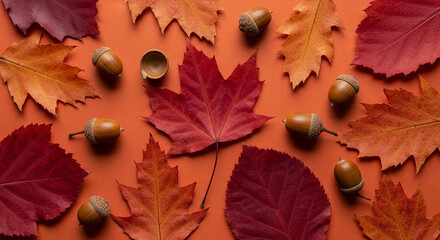 Autumnal arrangement of red and orange leaves and acorns on an orange background, showcasing fall colors and textures, ideal for seasonal designs