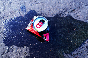 Spilled drink from Crumpled Beer Can. Discarded broken carbonated drink tin can on asphalt road. Thrown out Crushed juce. Crumpled soda can on asphalt with drink spilled. Crushed bottle.
