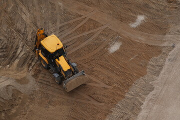 Yellow excavator leveling sandy soil at construction site with visible tire tracks