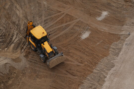 Yellow excavator leveling sandy soil at construction site with visible tire tracks
