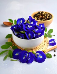 Fresh, vibrant blue pea flowers in white bowl, with tea and leaves