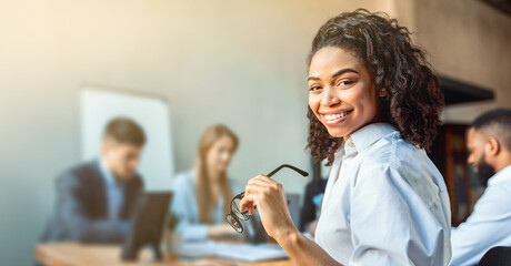 African American Business Lady Sitting On Corporate Meeting With Partners Smiling To Camera In Modern Office. Empty Space