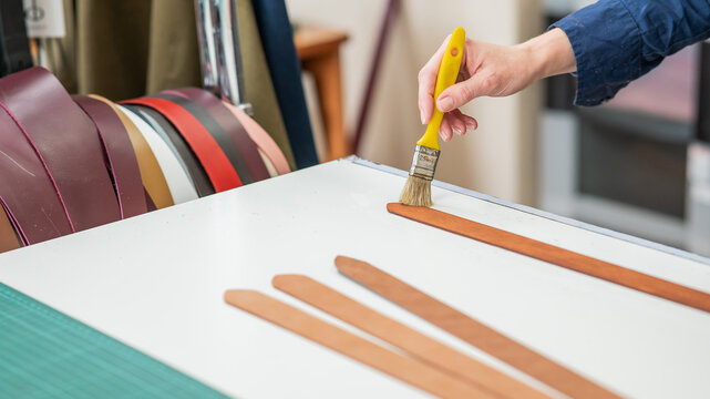 A craftsman uses a brush to cover leather parts. - Powered by Adobe