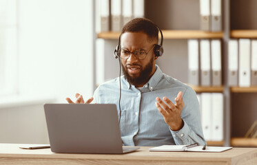 Disgruntled shocked sad young african american bearded male in glasses, headphones gestures and...