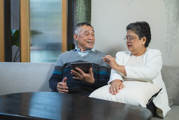 Elderly couple man and woman sit on sofa in cozy living room, use tablet together. appear be engaged in activity on tablet, possibly read browse internet plan your life, business or health insurance.