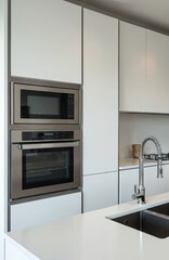 Fototapeta premium Modern kitchen features integrated stainless steel oven, microwave unit above sleek white cabinets. Double sink with chrome faucet, minimalist countertop. Contemporary interior design for residential