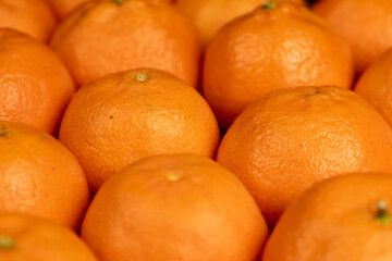 Unpeeled orange tangerines stacked together, a lot of ripe orange tangerines on the table
