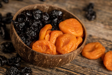 orange dried apricots and black prunes made from ripe blue plums mixed together in a plate , dried plums and apricots in a bowl made from natural materials