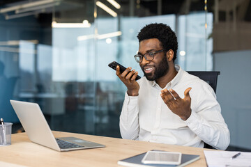 Smiling businessman recording voice message using smartphone in office