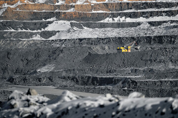 Open-pit coal mining in winter landscape with snow-covered terraces and yellow excavator