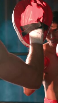 Asian and Caucasian Muay Thai boxer unleash punch in fierce boxing training session, delivering punching strike to sparring trainer, showcasing Muay Thai boxing technique and skill. Impetus