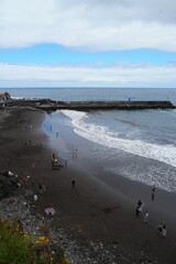Waves gently kiss the shore at Madeira Seixal Beach while visitors enjoy the coastal escape on a cloudy day in Portugal