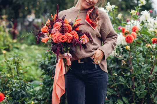 Fall flower arrangement. Close up of autumnal bouquet of orange dahlia flowers, burgundy red amaranth in female hands outdoors - Powered by Adobe