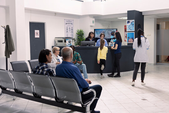 Multiethnic group of patients seated in hospital emergency room, awaiting for medical appointments. Calm, professional clinic atmosphere as sick individuals and visitors sit in waiting area.