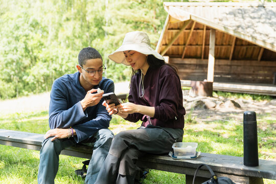 Hikers Taking a Break and Checking Phone on Outdoor Bench