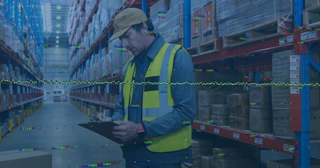 Inspecting worker wearing safety vest and hard hat holding clipboard in warehouse aisle with racks