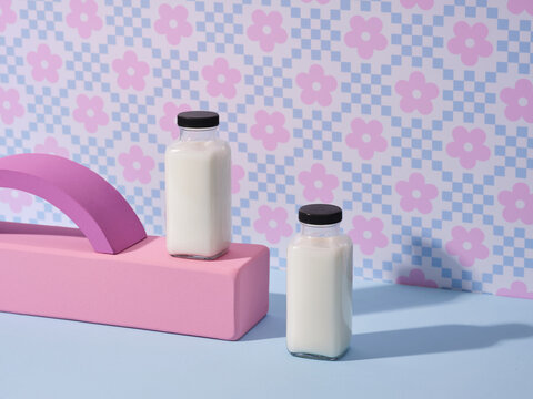 Two milk bottles arranged on a pink platform, with floral background