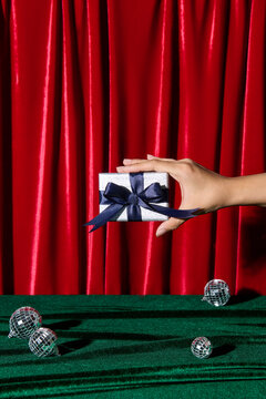 Hand Holding Gift Box with Navy Ribbon Against Red Curtain