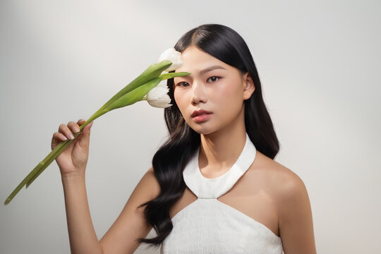 A stunning asian woman with dark hair delicately holds white tulips