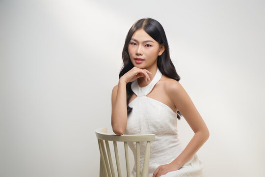 A stunning asian woman poses gracefully in a white dress
