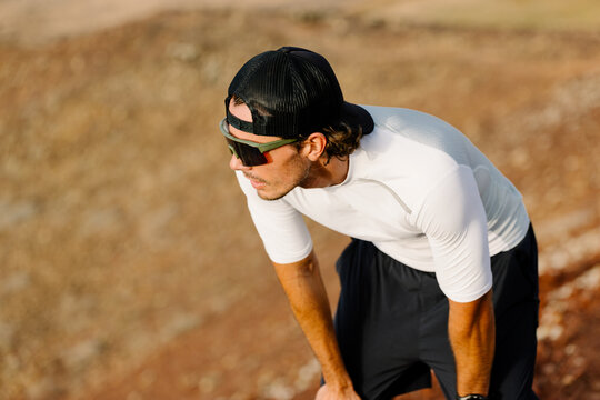 Mid shot of a trail runner leaning on knees resting atop a hill