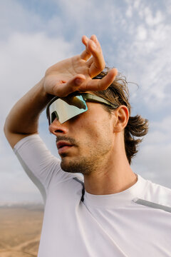 An athlete wearing sunglasses, wiping sweat from his forehead