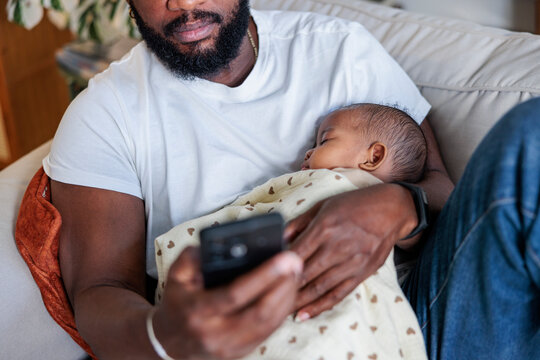 Father holds sleeping baby while using phone.