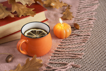 Cozy autumn mood with cup of tea with lemon, pumpkin-shaped candle and autumn leaves
