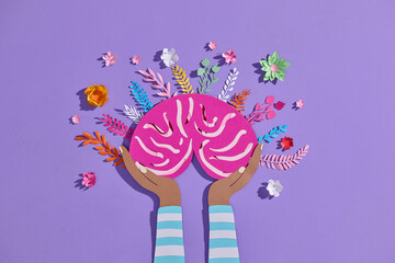 A paper brain held in hands, surrounded by colorful paper flowers